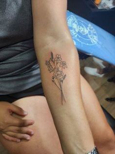 a woman with a flower tattoo on her arm sitting down and holding onto another person's leg