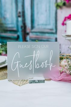 a sign sitting on top of a table next to a white plate with flowers in it