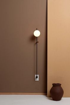 a brown vase sitting next to a wall with a light on it's side