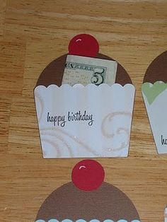 three cupcakes with happy birthday cards attached to them on top of a wooden table