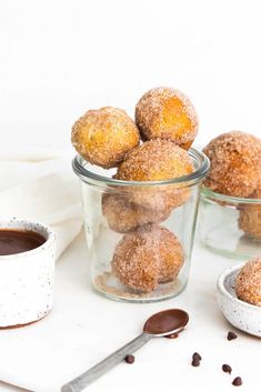 some sugared donuts are in small glass bowls next to a cup of coffee