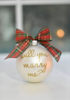 a white ornament with a red and green bow on it that says, will you marry me?