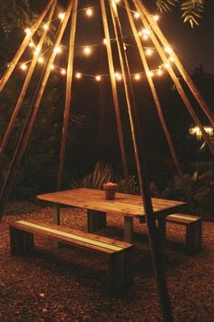 a wooden table and bench under a lit up teepee