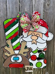 a christmas door hanger with a santa clause and reindeer on it, hanging from a wooden fence