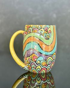 a colorful coffee cup sitting on top of a glass table next to a gray wall