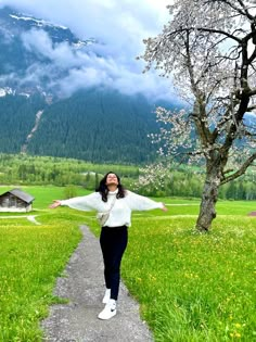 a woman standing on a path in the middle of a field with mountains behind her