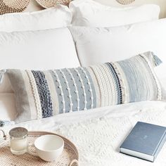 a white bed topped with pillows next to a tray filled with cups and saucers