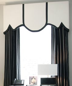 a window with black and white drapes in front of it, next to a desk