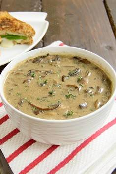 a bowl of mushroom soup on a red and white striped napkin with a sandwich in the background