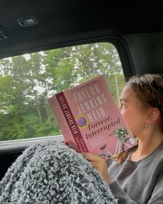 a woman sitting in the back seat of a car reading a book