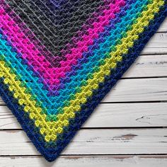 a multicolored crocheted triangle sits on a wooden surface