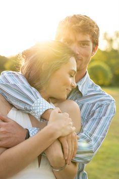 a man and woman embracing each other in a field with the sun shining on them