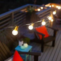 some lights that are on the side of a wooden deck with two chairs and a table