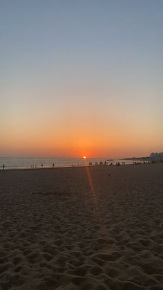 the sun is setting at the beach with people on it