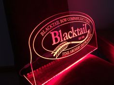 a blacktail illuminated sign sitting on top of a red couch in a dark room