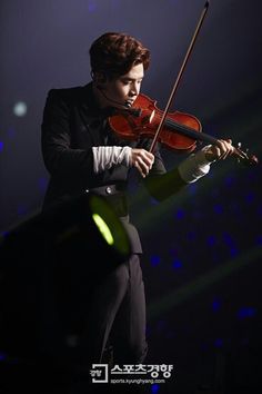 a man in a tuxedo playing a violin on stage with lights behind him