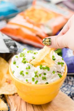 a person dipping some chips into a bowl of dip with sour cream and chives