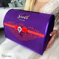 a woman in a wedding dress holding a purple box with an orange ribbon on it