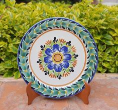 a blue and green plate sitting on top of a wooden stand next to some bushes