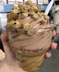 a person holding a cup filled with ice cream and chocolate chip cookie doughnuts