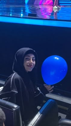 a woman in a black hoodie holding a blue balloon and smiling at the camera