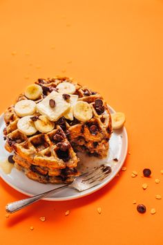 a waffle topped with bananas and chocolate chips on an orange table next to a fork