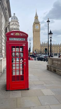 a red phone booth sitting on the side of a street next to a clock tower