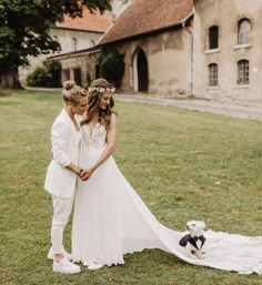 a bride and groom standing in front of an old building with a dog on the grass