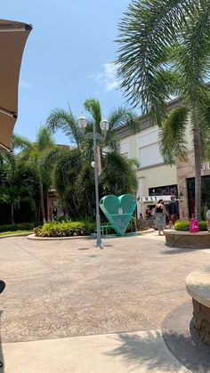 an open umbrella sitting on the side of a road next to palm trees and people