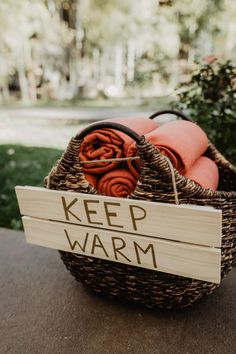 a basket filled with orange towels sitting on top of a wooden sign that says keep warm