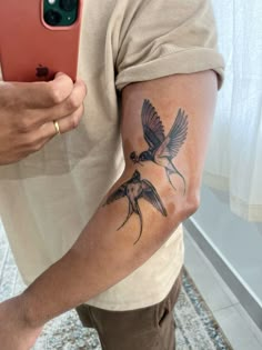 a man with a bird tattoo on his arm holding a cell phone and taking a selfie