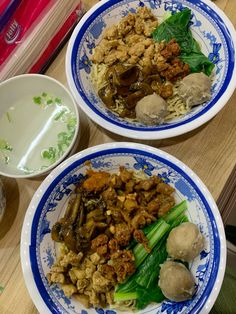 two blue and white plates filled with food on top of a wooden table next to bowls