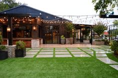 an outdoor patio with string lights and potted plants on the grass in front of it