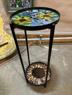 a small table with a glass top and metal stand on the floor next to a vase