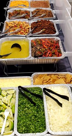 several trays of food are lined up on a buffet table with utensils