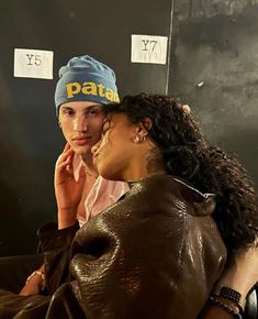 two women sitting next to each other in front of a wall with stickers on it