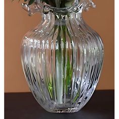 a clear vase filled with flowers on top of a wooden table in front of a brown wall