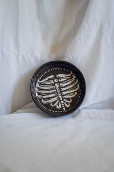 a black and white plate with a skeleton on it's side sitting on a bed