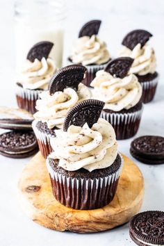 chocolate cupcakes with white frosting and oreo cookies on a cutting board