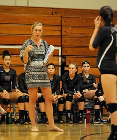 the volleyball team is watching as their coach gives instructions to her players on the sideline