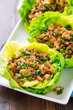 three lettuce cups filled with meat and vegetables on a white plate next to a blue napkin