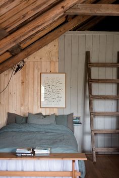 a bed in a room with wooden walls and a ladder hanging from the ceiling next to it