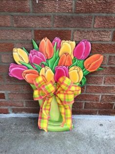 a vase filled with colorful flowers sitting on top of a cement floor next to a brick wall