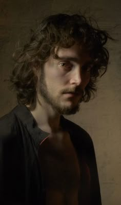 a man with long curly hair standing in front of a wall