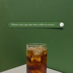 a glass filled with ice sitting on top of a table next to a sign that says, where can i get the best coffee in town?