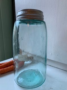 a glass jar filled with water next to two carrots on a white counter top