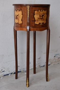 an antique wooden table with two drawers and gold trimmings on the top, against a white wall