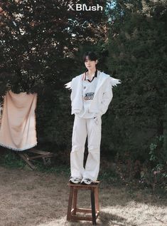 a woman standing on top of a wooden stool in front of some trees and bushes