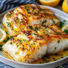 some fish on a white plate with lemons and parmesan cheese garnish