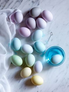 several different colored eggs sitting next to each other on a marble counter top with a blue cup